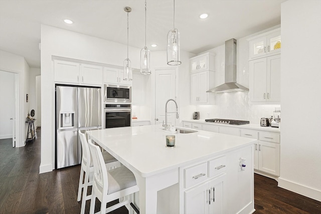 kitchen featuring wall chimney range hood, sink, appliances with stainless steel finishes, an island with sink, and white cabinets