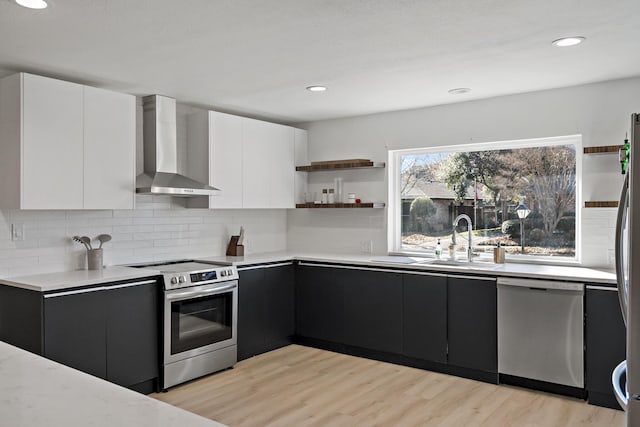 kitchen with wall chimney range hood, sink, light hardwood / wood-style flooring, stainless steel appliances, and white cabinets