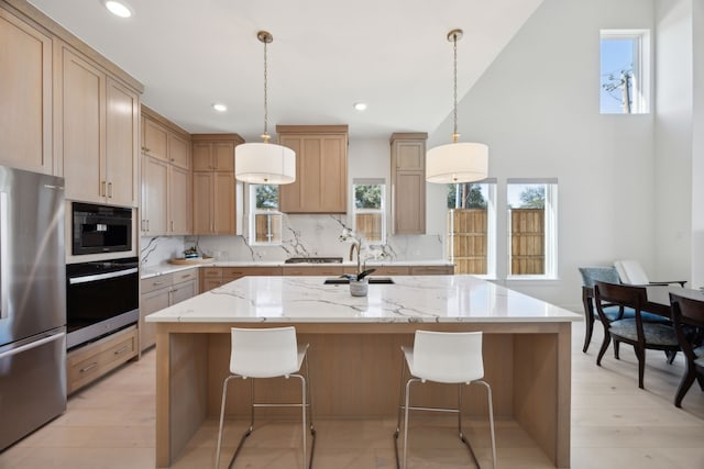 kitchen with appliances with stainless steel finishes, decorative backsplash, hanging light fixtures, a kitchen island with sink, and light stone counters