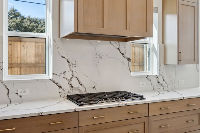 kitchen with stainless steel gas stovetop, backsplash, and light stone counters