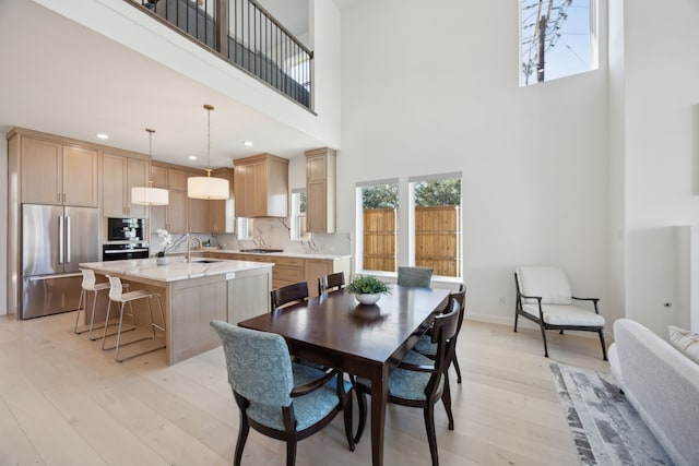 dining room with sink, a towering ceiling, and light hardwood / wood-style floors