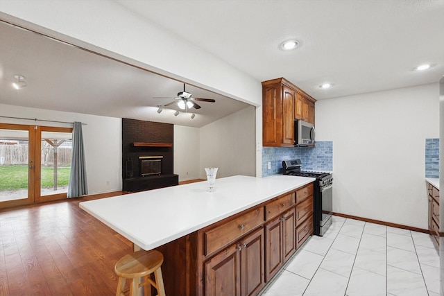 kitchen featuring vaulted ceiling with beams, a breakfast bar area, backsplash, stainless steel appliances, and a brick fireplace