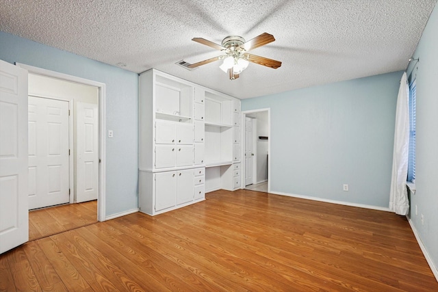 unfurnished bedroom with ceiling fan, built in desk, a textured ceiling, and light wood-type flooring