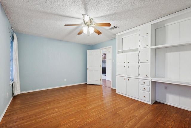 unfurnished bedroom featuring hardwood / wood-style floors, built in desk, a textured ceiling, and ceiling fan