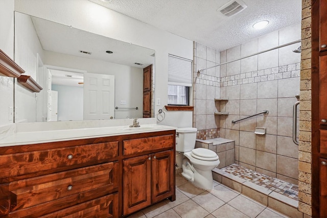 bathroom featuring a tile shower, tile patterned flooring, vanity, toilet, and a textured ceiling