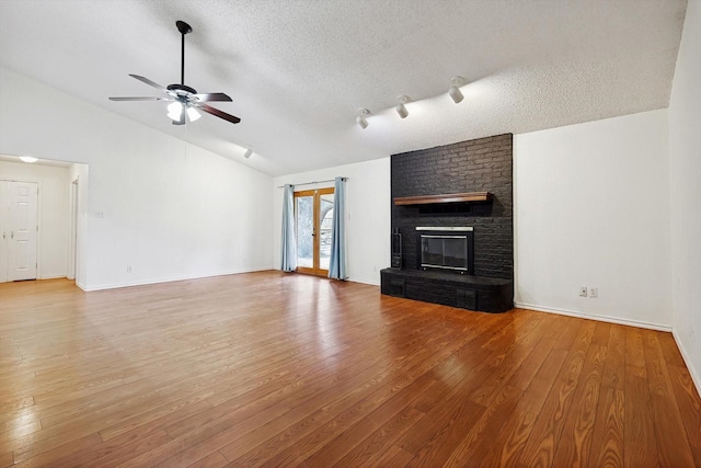 unfurnished living room with wood-type flooring, lofted ceiling, ceiling fan, a brick fireplace, and a textured ceiling