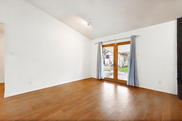 spare room with wood-type flooring, vaulted ceiling, and a textured ceiling