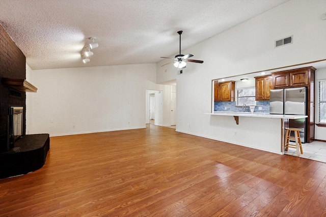 living room with high vaulted ceiling, a textured ceiling, hardwood / wood-style flooring, ceiling fan, and a fireplace