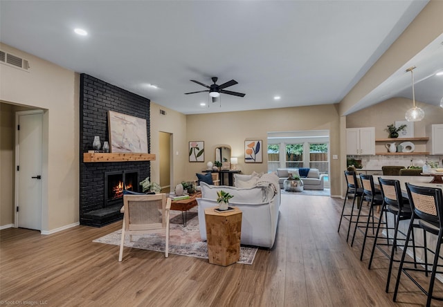 living room with ceiling fan, a brick fireplace, and light wood-type flooring