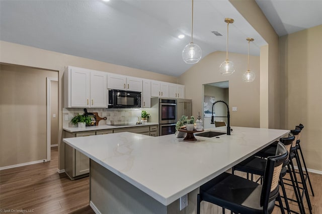 kitchen featuring pendant lighting, sink, backsplash, black appliances, and a large island with sink