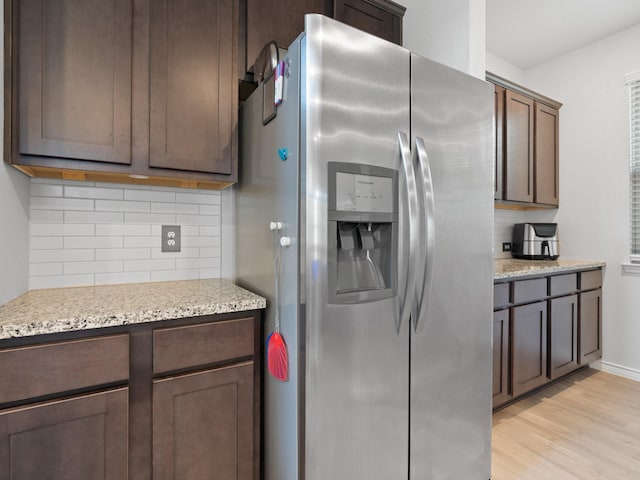 kitchen with tasteful backsplash, dark brown cabinets, stainless steel fridge, light stone countertops, and light hardwood / wood-style floors