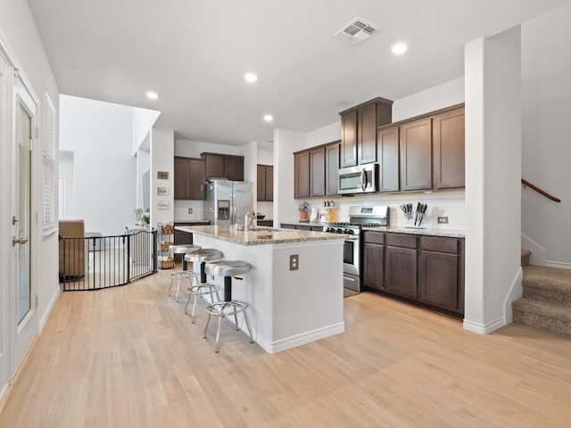 kitchen featuring sink, a breakfast bar area, light wood-type flooring, stainless steel appliances, and a kitchen island with sink