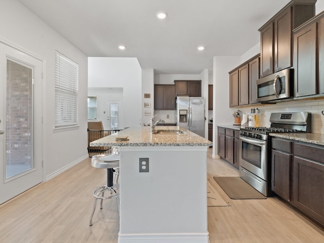 kitchen with stainless steel appliances, sink, a center island with sink, and light hardwood / wood-style flooring