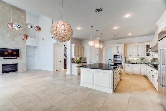 kitchen with appliances with stainless steel finishes, pendant lighting, a fireplace, backsplash, and a center island with sink