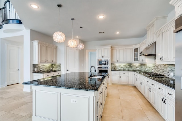 kitchen featuring hanging light fixtures, a center island with sink, appliances with stainless steel finishes, decorative backsplash, and exhaust hood