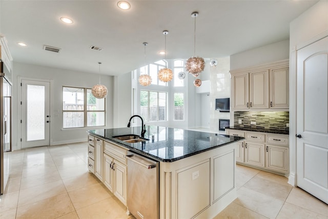 kitchen featuring sink, a center island with sink, dark stone counters, and cream cabinetry