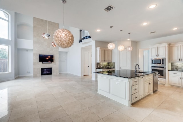 kitchen with stainless steel appliances, an island with sink, hanging light fixtures, and backsplash