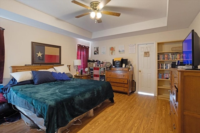 bedroom featuring light wood-type flooring, ceiling fan, and a tray ceiling