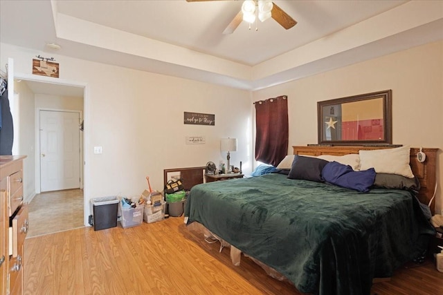 bedroom featuring light hardwood / wood-style floors, ceiling fan, and a tray ceiling