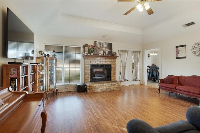 living room featuring a brick fireplace, wood-type flooring, and ceiling fan