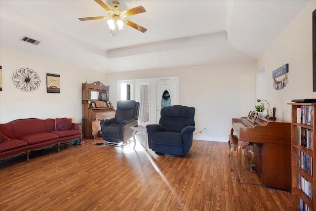 living room with hardwood / wood-style flooring, ceiling fan, and a tray ceiling