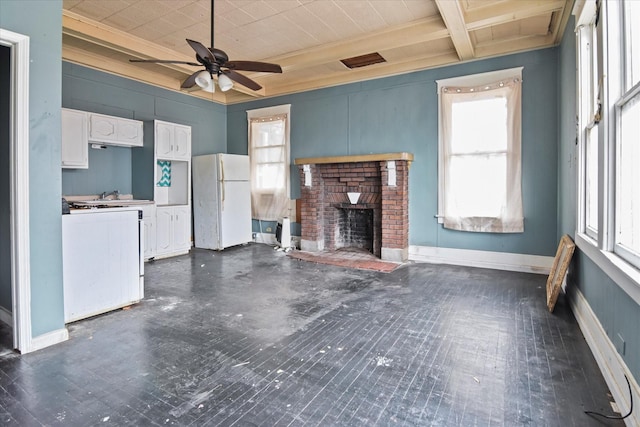 unfurnished living room featuring beamed ceiling, ceiling fan, a healthy amount of sunlight, and a brick fireplace