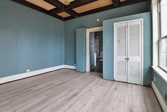 unfurnished bedroom with beamed ceiling, coffered ceiling, light hardwood / wood-style floors, and a closet