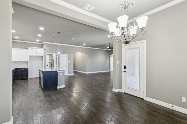 kitchen featuring white cabinetry, pendant lighting, light stone countertops, a kitchen island with sink, and decorative backsplash