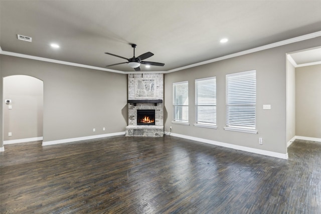 unfurnished living room featuring ornamental molding, a stone fireplace, dark wood-type flooring, and ceiling fan