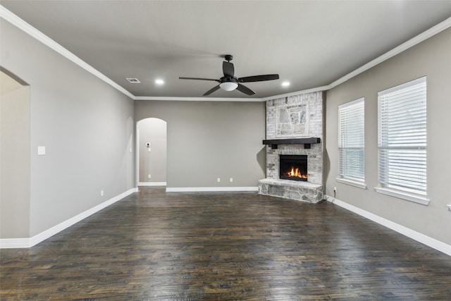 unfurnished living room featuring crown molding, ceiling fan, a stone fireplace, and dark hardwood / wood-style flooring