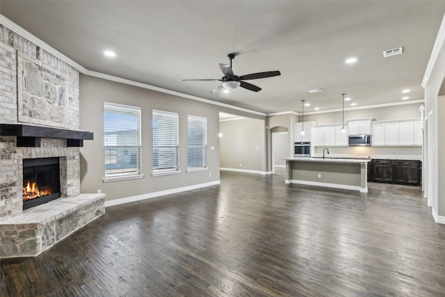 unfurnished living room with a stone fireplace, dark hardwood / wood-style floors, sink, and ceiling fan