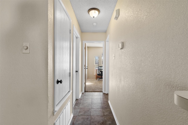 hallway with a textured ceiling and dark colored carpet