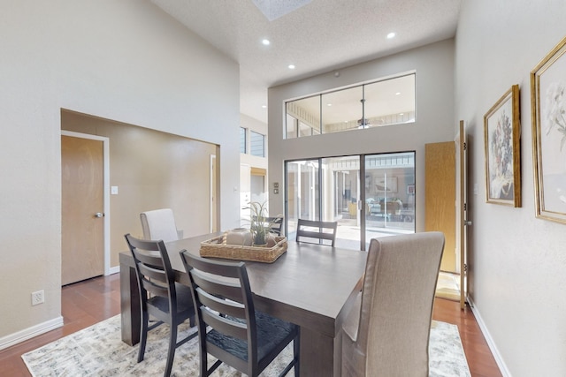 dining area featuring hardwood / wood-style floors, a towering ceiling, and a textured ceiling