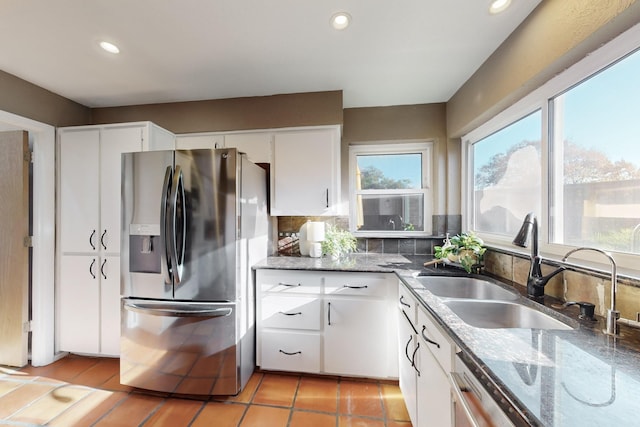 kitchen with sink, dark stone countertops, white cabinets, light tile patterned flooring, and stainless steel fridge with ice dispenser