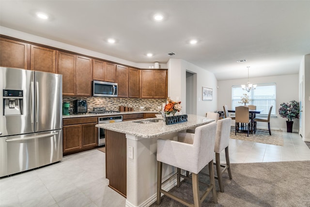 kitchen featuring a kitchen bar, light stone counters, hanging light fixtures, a center island with sink, and stainless steel appliances