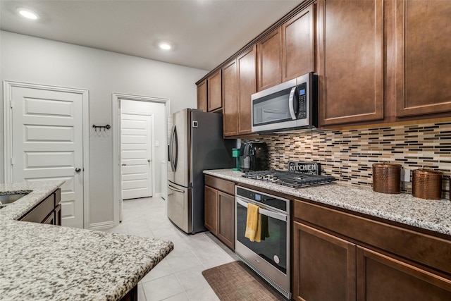 kitchen featuring light tile patterned floors, dark brown cabinets, stainless steel appliances, light stone counters, and decorative backsplash