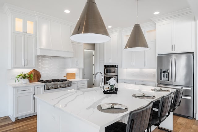 kitchen with stainless steel appliances, a kitchen breakfast bar, white cabinetry, and premium range hood