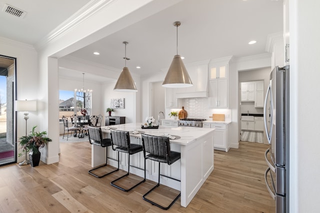 kitchen with visible vents, freestanding refrigerator, range, white cabinetry, and custom range hood