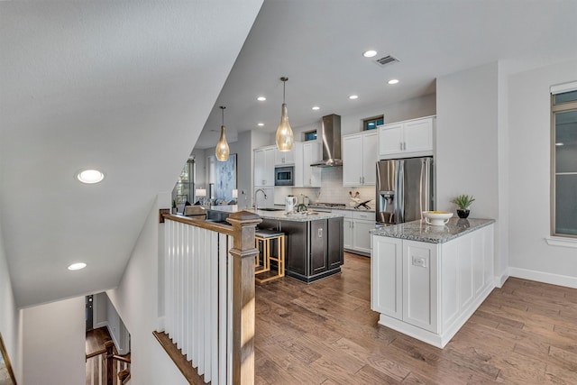 kitchen with white cabinetry, stainless steel appliances, a kitchen bar, decorative light fixtures, and wall chimney exhaust hood