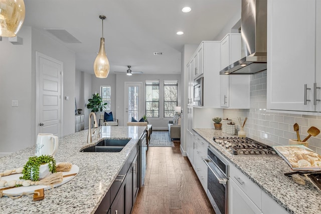 kitchen featuring wall chimney range hood, sink, stainless steel appliances, light stone counters, and white cabinets