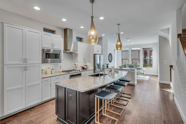 kitchen featuring white cabinetry, stainless steel appliances, wall chimney exhaust hood, and a center island with sink