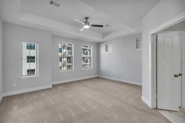 spare room with ceiling fan, a raised ceiling, and light carpet