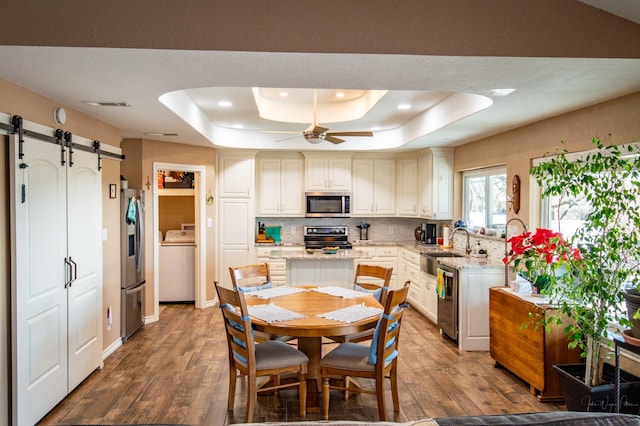 kitchen with washer / clothes dryer, wood-type flooring, stainless steel appliances, a raised ceiling, and a barn door