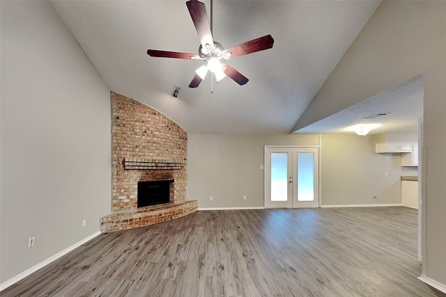 unfurnished living room with lofted ceiling, light hardwood / wood-style floors, a textured ceiling, a brick fireplace, and french doors