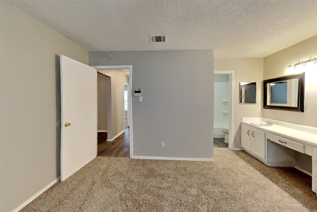 unfurnished bedroom with built in desk, ensuite bath, sink, light carpet, and a textured ceiling