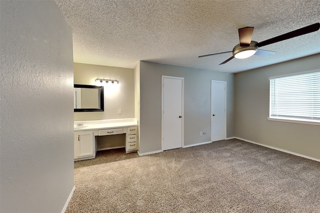 unfurnished bedroom with two closets, built in desk, ceiling fan, light carpet, and a textured ceiling