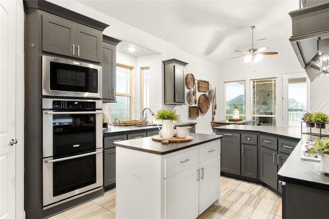 kitchen with gray cabinets, vaulted ceiling, a kitchen island, sink, and stainless steel appliances