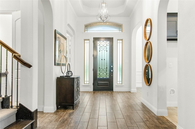 entryway with crown molding, a wealth of natural light, a notable chandelier, and a tray ceiling