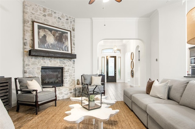 living room featuring crown molding, ceiling fan, a stone fireplace, and light hardwood / wood-style flooring