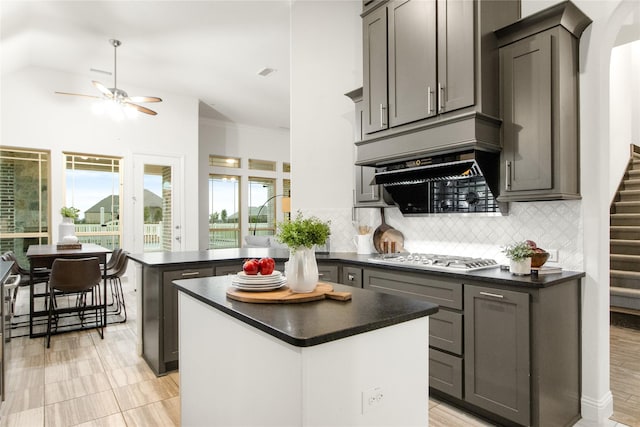 kitchen with gray cabinets, tasteful backsplash, a center island, stainless steel gas cooktop, and ceiling fan